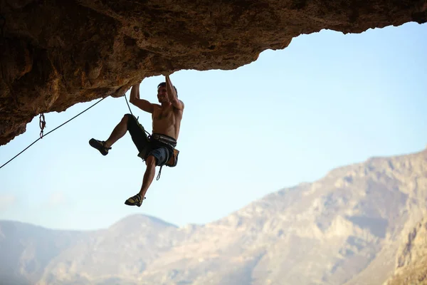 Genç adam tırmanma devam edebilmek için Cliff ulaşmaya — Stok fotoğraf