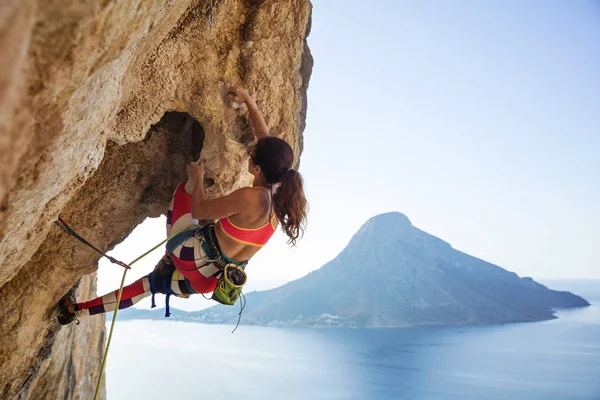 Young woman struggling to climb ledge on cliff — Stock Photo, Image