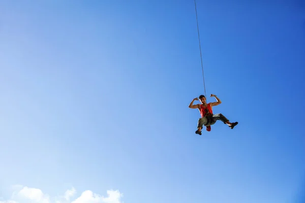 Rock climber swinging on rope and flexing muscles — Stock Photo, Image