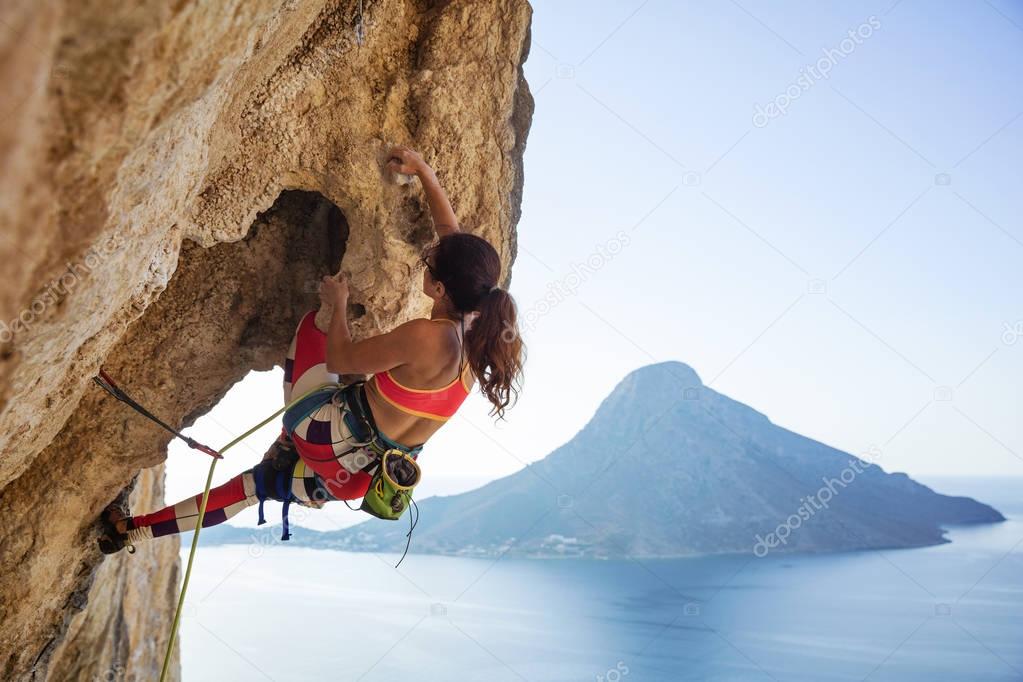 Young woman struggling to climb ledge on cliff