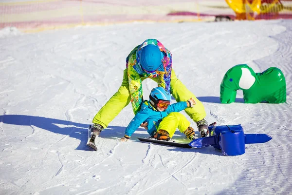 Father helping little get on feet after fall on ski slope — Stock Photo, Image