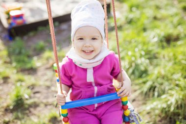 Bahar bahçesinde salıncakta sallanan mutlu küçük kız. Güzel kız kameraya bakıyor ve gülümsüyor..