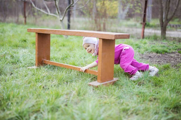 快乐的小女孩在春天花园的木制长椅下玩躲猫猫 — 图库照片