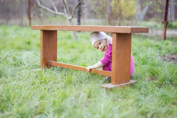 Happy Little Girl Odgrywa Peekaboo Pod Drewnianą Ławką Ogrodzie Wiosna — Zdjęcie stockowe