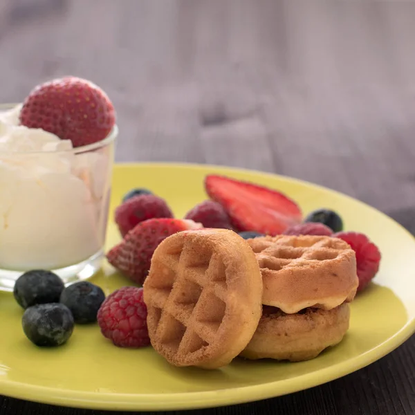 A glass of whipped cream, next to it are waffles with raspberries, blueberries and strawberries. — Stock Photo, Image