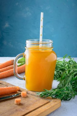 Havuç suyu ve sebze alışılmadık bir mavi arka plan üzerinde güzel kompozisyon bir kavanoz ile. Yararlı veggie içki.