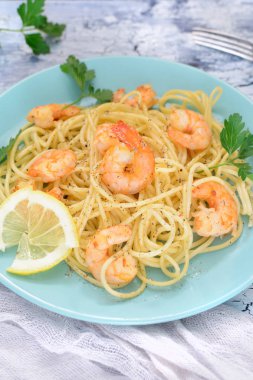 Spagetti karides, limon ve maydanoz ile süslenmiş ile lezzetli bir tarif. Mavi bir tabak bir tabak.