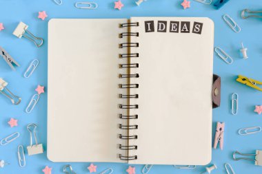 Açık defter Kırtasiye karışıklık ortasında yaylar üzerinde. Beyaz sayfa üzerinde yazıt fikir. Klipleri, büro düğmeleri ve mavi bir arka plan üzerinde dağınık yıldız.