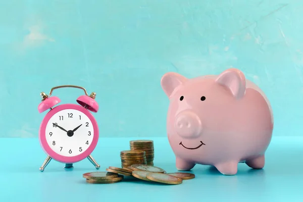 Стеки и куча монет, розовый будильник и копилка на бирюзовом фоне. Символ накопления денег . — стоковое фото