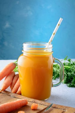 Havuç suyu ve sebze alışılmadık bir mavi arka plan üzerinde güzel kompozisyon bir kavanoz ile. Yararlı veggie içki.