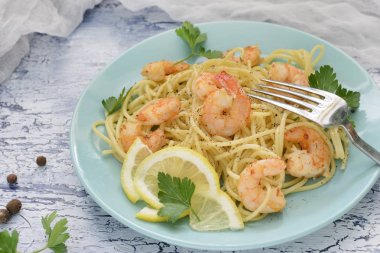 Spagetti karides, limon ve maydanoz ile süslenmiş ile lezzetli bir tarif. Mavi bir tabak bir tabak.