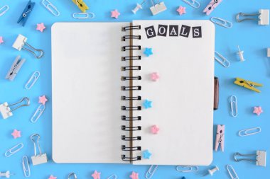 Pnotebook beyaz çarşaflı yaylar üzerinde. Yazıt gol. Klipleri, büro düğmeleri ve yıldız bir karmaşa mavi bir arka plan üzerinde.