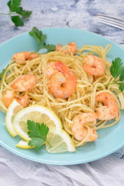 Lezzetli bir spagetti karides tarifi, limon ve kruvasan ile dekore edilmiştir. Güzel mavi tabakta yemek hazır.