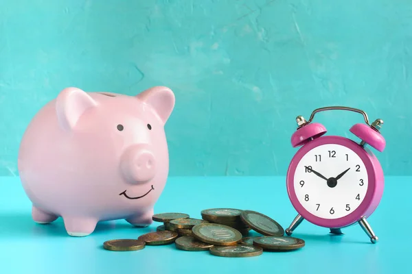 Piggy bank on a blue background. Near a pile of coins and a pink alarm clock. The symbol is the accumulation and conservation of money.