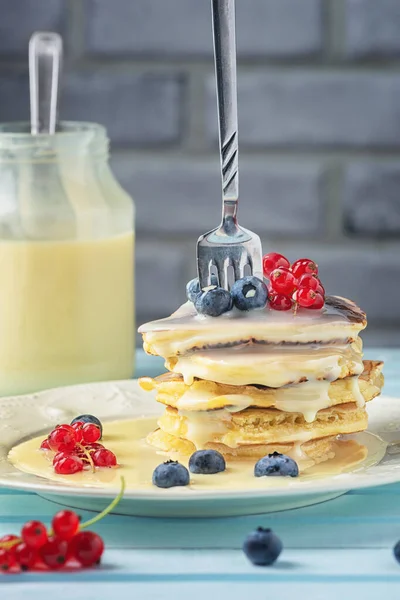 Freshly made pancakes with condensed milk. A fork is inserted into the stack of pancakes. Tasty breakfast with fresh berries — Stock Photo, Image