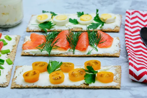 Little snacks with different ingredients. Crispy bread sandwiches with curd cheese, trout, tomato and dill. Light summer snack — Stock Photo, Image