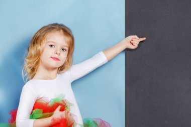 Güzel, şirin bir bebek pozu. Sarı saçlı küçük bir kız siyah arka plandaki boş bir yeri işaret ediyor..