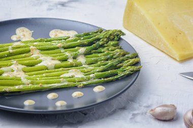 Siyah bir tabakta taze haşlanmış yeşil kuşkonmaz var. Fıstık soslu ve parmesanlı sağlıklı bir diyet tarifi.
