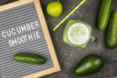 Koyu bir arka planda bir kavanoz taze sıkılmış yeşil meyve suyu. Avokado ve salatalıktan yapılmış sağlıklı bir smoothie. Üzerinde yazı olan bir keçeli tahta, metin için bir yer