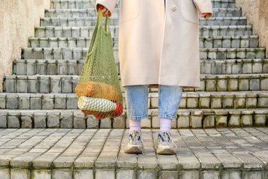 Ceket giymiş bir kız merdivenlerde duruyor, elinde alışveriş torbası olan bir bez torbası var. Sıfır kayıp. Kesilmiş fotoğraf
