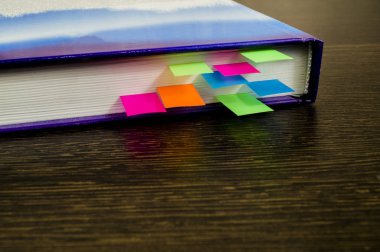 Mavi kitap ahşap bir masa üzerinde renkli yer imleri ile