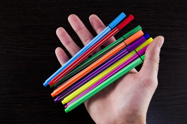 Marcadores multicolores en una mano sobre una mesa de fondo oscuro —  Fotos de Stock
