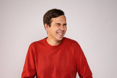 Kırmızı kazaklı genç bir adam gülüyor. Açık arkaplanda portre