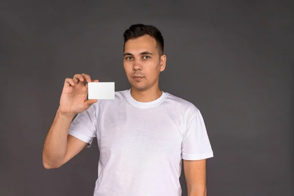 Молодий чоловік у білій футболці тримає візитку — стокове фото