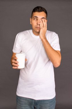 Beyaz tişörtlü bir adam kahve içiyor ve uyanıp neşelenmeye çalışıyor..