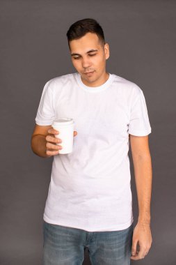 Beyaz tişörtlü bir adam kahve içiyor ve uyanıp neşelenmeye çalışıyor..