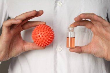 Bir tıp çalışanı koronavirüsün bir modelini elinde tutuyor. Gri arkaplanda fotoğraf