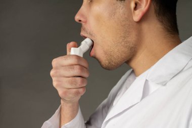 Bir insan hastalığı yenmek için öksürük spreyi kullanır. Gri arkaplanda fotoğraf