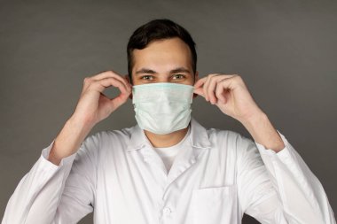 Doktor kendini yeni bir virüsten korumak için maske takıyor. Coronavirüs. Gri arkaplanda fotoğraf