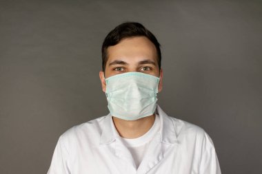 Tıbbi önlüklü ve koruyucu maskeli bir doktorun portresi. Gri arkaplanda fotoğraf