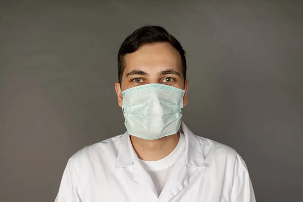 Portrait of a doctor in a medical gown and protective mask. Photo on a grey background