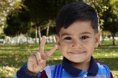 Gülümseyen genç küçük çocuk bir zafer işareti verir