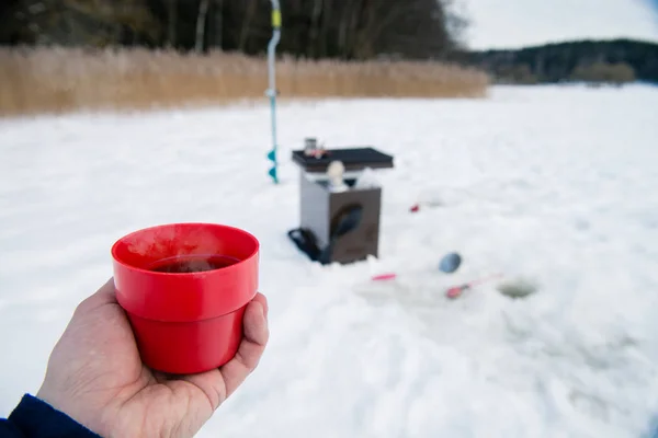 Горячий чай в руке рыбака, пикник на ледяной рыбалке — стоковое фото