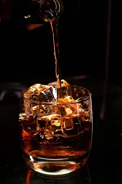 El whisky de alcohol fuerte se vierte en un vaso con cierre de hielo. — Foto de Stock