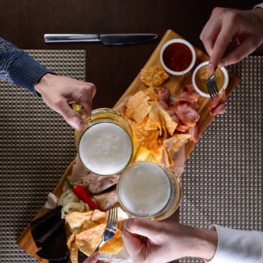 İki erkek el elinde bira bardaklarıyla kafede bir masada oturuyor..