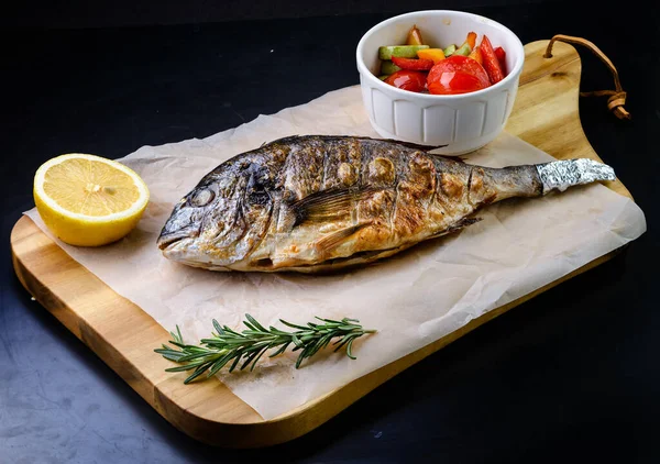 Delicious grilled dorado or sea bream fish with slices, spices, grilled dorada on a wooden board