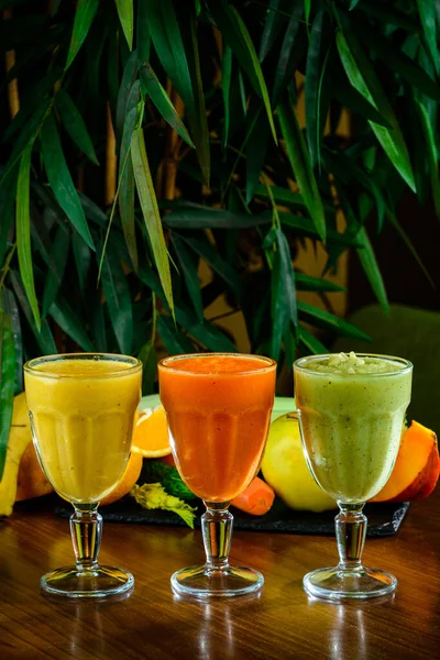 Healthy vegetable and fruit juices or smoothie in glass, ripe slices of orange, apple, carrot, celery, avocado, Orange, green, red colored smoothies freshly squeezed juice