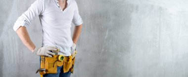 Kurulum kemeri olan beyaz gömlekli inşaat işçisi mühendisi. Beton duvardaki tamirci aletinde yazı için yer var.