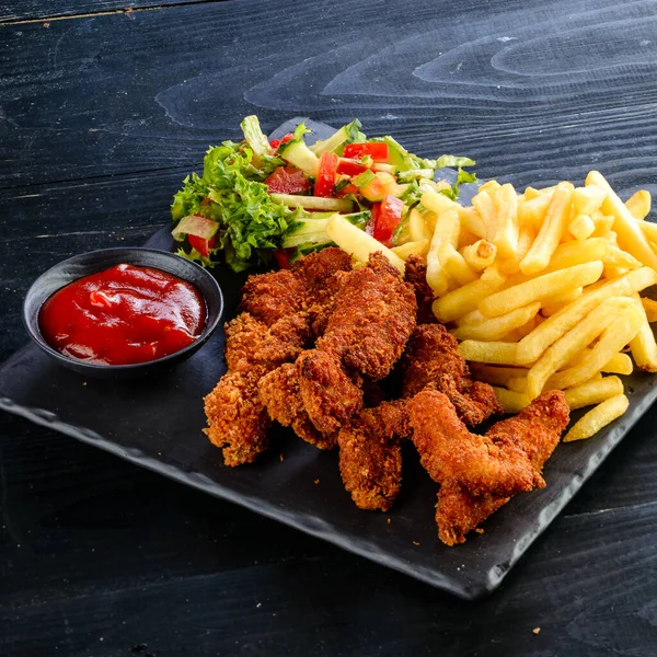 Fried chicken, nuggets and french fries, set of chicken nuggets, salad and french fries on wood table. Food issue.