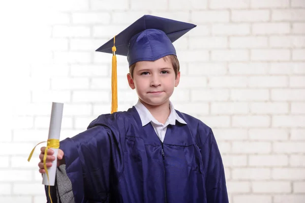 Basisschool jongen in de cup en jurk poseren met diploma. — Stockfoto