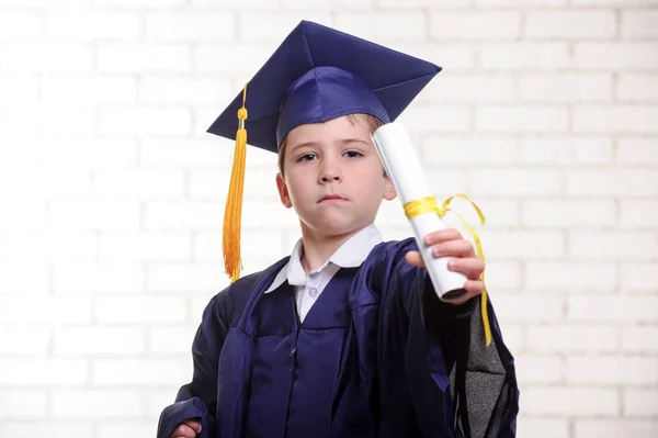 Basisschool jongen in de cup en jurk poseren met diploma. — Stockfoto