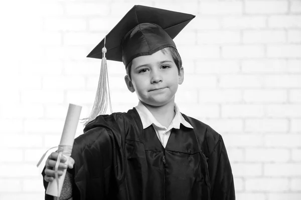 Мальчик начальной школы в кубке и халате позирует с дипломом . — стоковое фото