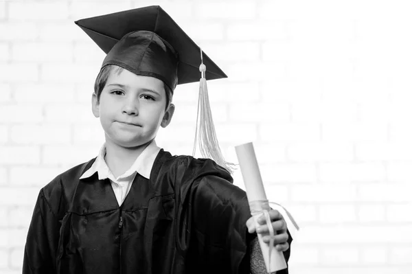 Мальчик начальной школы в кубке и халате позирует с дипломом — стоковое фото