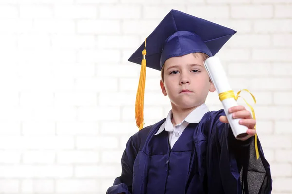 Primary school boy in cup and gown posing with his finger — Stock Photo, Image