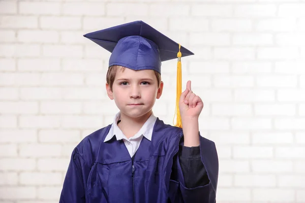 Basisschool jongen in de cup en jurk poseren met diploma. — Stockfoto