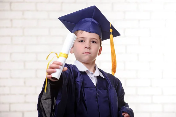 Basisschool jongen in de cup en jurk poseren met diploma. — Stockfoto